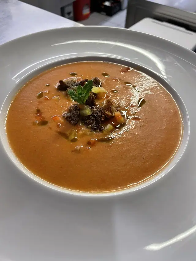 Gazpacho in einem weissen Suppenteller, garniert mit Gemüsewürfeln und Kräutern