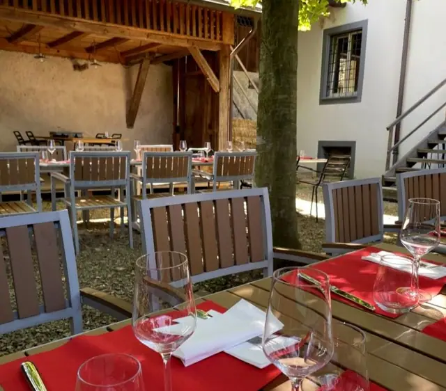 Gedeckte Tische mit roten Sets im Innenhof, im Hintergrund der Holzbau und der Stamm der Platane