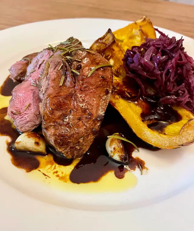 Rosa gebratenes Fleisch mit Rotkraut, geröstetem Kürbis und dunkler Sauce