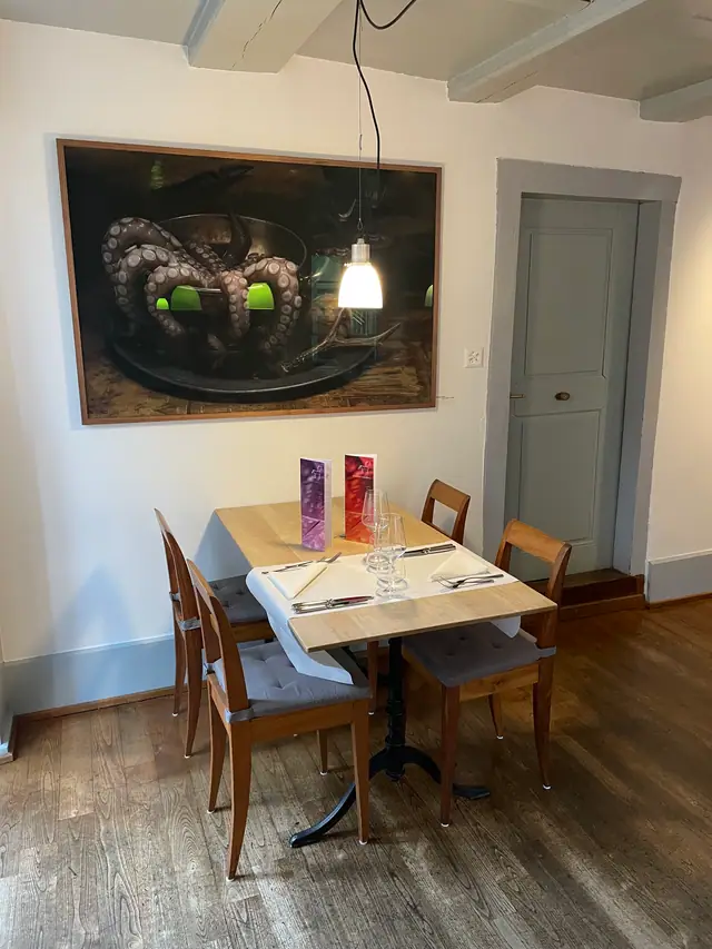 Ein grosses Oktopus-Bild an der weissen Wand über einem gedeckten Tisch, daneben eine graue Tür