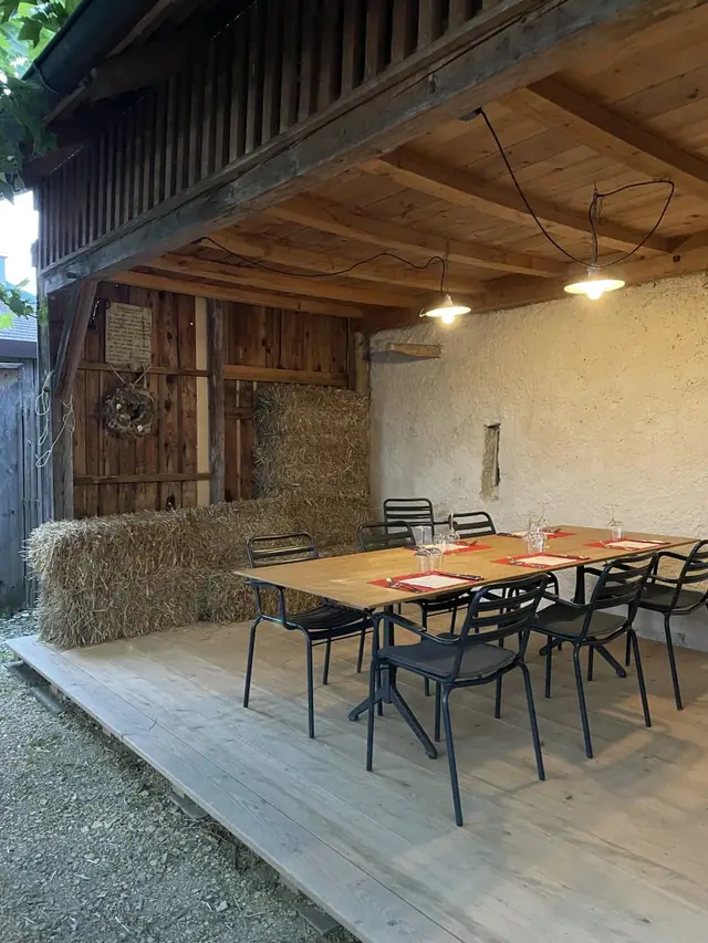 Das Schöpfli: überdachter Sitzplatz mit langem Holztisch, Strohballen und Holzwand