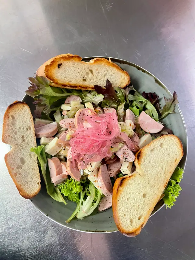 Wurstsalat mit roten Zwiebeln und Blattsalat in einer Schale, dazu geröstetes Brot